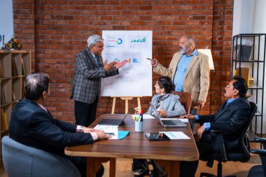 Hintli üst düzey iş adamları modern ofiste tartışırken Hintli üst düzey Asyalı iş adamları şirket büyümesi, strateji ve dizüstü bilgisayarla çalışırken masadaki kağıtlar hakkında hararetli tartışmalara girişiyorlar.