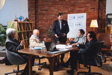 Hintli iş adamları projeyi tartışırken sunucu ayakta duruyor. Hintli iş adamı kıdemli yönetici ekibine stratejiyi açıklıyor.