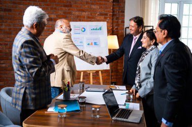 Hintli iş adamları anlaşmadan sonra el sıkışıyor. Hintli kıdemli Asyalı işadamı modern ofis toplantılarında gülümserken başarılı bir anlaşmayı imzalıyor.