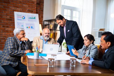 Hintli üst düzey iş adamları, Hindistan 'da üst düzey Asyalı iş adamları olarak birlikte çalışarak, rahat, modern kurumsal işyerlerindeki görevleri incelerken dizüstü bilgisayarları ve masa başındaki kağıtları kullanarak iş birliği yapıyorlar.