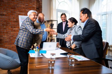 Hintli iş adamları anlaşmadan sonra el sıkışıyor. Hintli kıdemli Asyalı işadamı modern ofis toplantılarında gülümserken başarılı bir anlaşmayı imzalıyor.