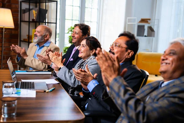 Hintli beş iş adamı sunum ve alkışları Hintli üst düzey Asyalı iş adamlarına yakın plan olarak görüyor ve modern ofis içinde masada otururken veya ayakta dururken başarılı brifing veriyorlar.