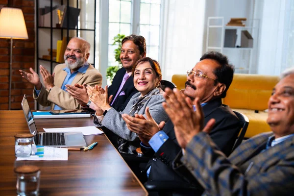 Hintli beş iş adamı sunum ve alkışları Hintli üst düzey Asyalı iş adamlarına yakın plan olarak görüyor ve modern ofis içinde masada otururken veya ayakta dururken başarılı brifing veriyorlar.