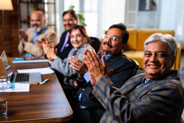 Hintli beş iş adamı sunum ve alkışları Hintli üst düzey Asyalı iş adamlarına yakın plan olarak görüyor ve modern ofis içinde masada otururken veya ayakta dururken başarılı brifing veriyorlar.