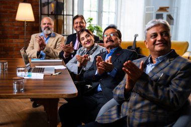 Hintli beş iş adamı sunum ve alkışları Hintli üst düzey Asyalı iş adamlarına yakın plan olarak görüyor ve modern ofis içinde masada otururken veya ayakta dururken başarılı brifing veriyorlar.