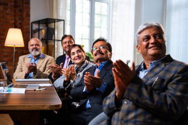 Hintli beş iş adamı sunum ve alkışları Hintli üst düzey Asyalı iş adamlarına yakın plan olarak görüyor ve modern ofis içinde masada otururken veya ayakta dururken başarılı brifing veriyorlar.