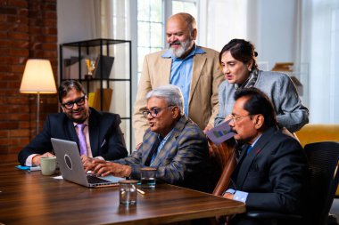 Hintli üst düzey iş adamları, Hindistan 'da üst düzey Asyalı iş adamları olarak birlikte çalışarak, rahat, modern kurumsal işyerlerindeki görevleri incelerken dizüstü bilgisayarları ve masa başındaki kağıtları kullanarak iş birliği yapıyorlar.