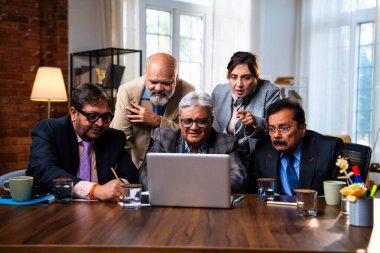 Hintli üst düzey iş adamları, Hindistan 'da üst düzey Asyalı iş adamları olarak birlikte çalışarak, rahat, modern kurumsal işyerlerindeki görevleri incelerken dizüstü bilgisayarları ve masa başındaki kağıtları kullanarak iş birliği yapıyorlar.