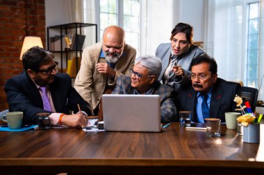 Hintli üst düzey iş adamları, Hindistan 'da üst düzey Asyalı iş adamları olarak birlikte çalışarak, rahat, modern kurumsal işyerlerindeki görevleri incelerken dizüstü bilgisayarları ve masa başındaki kağıtları kullanarak iş birliği yapıyorlar.