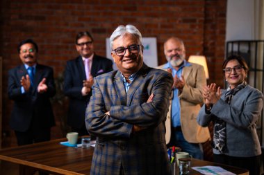 Hintli kıdemli iş adamının portresi Hintli üst düzey yönetici yönetici kameraya kendinden emin bir ifadeyle gülümserken meslektaşı modern kurumsal ofiste arkasında duruyor.