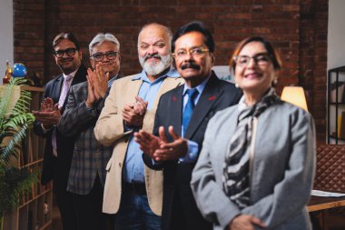 Hintli üst düzey iş adamlarının portresi gülümseyerek alkışlarken, Hintli üst düzey Asyalı yöneticiler modern şirket işyerindeki kameralara bakarak başarıyı alkışlıyor ve kutluyorlar.