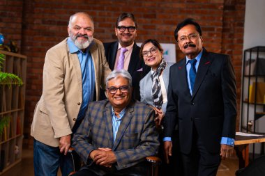 Hintli üst düzey iş adamlarının portresi Hintli üst düzey Asya yöneticileri kılığına girmiş patronun kanat koltuğunda otururken modern şirket ofisinde poz verirken kameraya gülümsüyor.