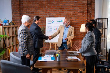 Hintli işadamları, Hindistan 'ın üst düzey Asyalı iş adamları olarak sunum yaparken el sıkışıyorlar. Yüksek yönetim, samimi modern ofis grafiği kullanarak başarılı büyüme projeksiyonunu kutluyor.