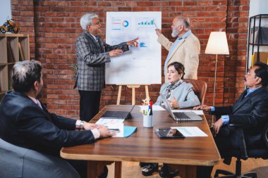 Hintli üst düzey iş adamları modern ofiste tartışırken Hintli üst düzey Asyalı iş adamları şirket büyümesi, strateji ve dizüstü bilgisayarla çalışırken masadaki kağıtlar hakkında hararetli tartışmalara girişiyorlar.