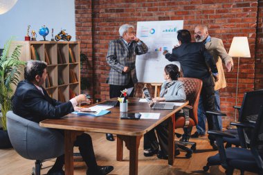 Hintli üst düzey iş adamları modern ofiste tartışırken Hintli üst düzey Asyalı iş adamları şirket büyümesi, strateji ve dizüstü bilgisayarla çalışırken masadaki kağıtlar hakkında hararetli tartışmalara girişiyorlar.