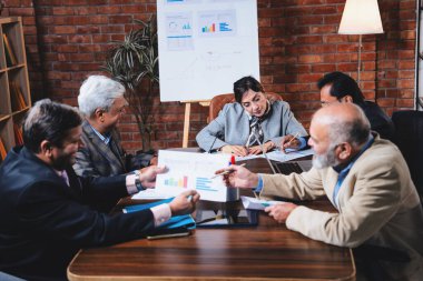 Hintli üst düzey iş adamları, Hindistan 'da üst düzey Asyalı iş adamları olarak birlikte çalışarak, rahat, modern kurumsal işyerlerindeki görevleri incelerken dizüstü bilgisayarları ve masa başındaki kağıtları kullanarak iş birliği yapıyorlar.