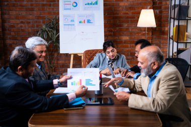 Hintli üst düzey iş adamları, Hindistan 'da üst düzey Asyalı iş adamları olarak birlikte çalışarak, rahat, modern kurumsal işyerlerindeki görevleri incelerken dizüstü bilgisayarları ve masa başındaki kağıtları kullanarak iş birliği yapıyorlar.