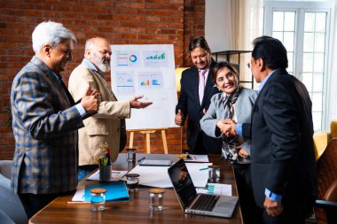 Hintli iş adamları anlaşmadan sonra el sıkışıyor. Hintli kıdemli Asyalı işadamı modern ofis toplantılarında gülümserken başarılı bir anlaşmayı imzalıyor.