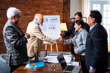 Hintli iş adamları anlaşmadan sonra el sıkışıyor. Hintli kıdemli Asyalı işadamı modern ofis toplantılarında gülümserken başarılı bir anlaşmayı imzalıyor.