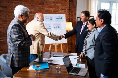 Hintli iş adamları anlaşmadan sonra el sıkışıyor. Hintli kıdemli Asyalı işadamı modern ofis toplantılarında gülümserken başarılı bir anlaşmayı imzalıyor.