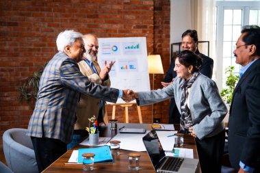 Hintli iş adamları anlaşmadan sonra el sıkışıyor. Hintli kıdemli Asyalı işadamı modern ofis toplantılarında gülümserken başarılı bir anlaşmayı imzalıyor.