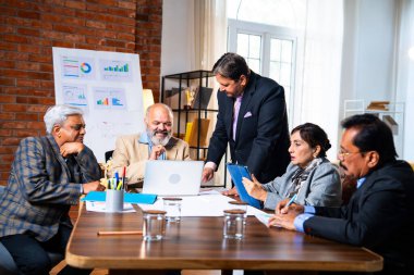 Hintli üst düzey iş adamları, Hindistan 'da üst düzey Asyalı iş adamları olarak birlikte çalışarak, rahat, modern kurumsal işyerlerindeki görevleri incelerken dizüstü bilgisayarları ve masa başındaki kağıtları kullanarak iş birliği yapıyorlar.