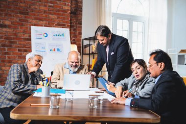 Hintli üst düzey iş adamları, Hindistan 'da üst düzey Asyalı iş adamları olarak birlikte çalışarak, rahat, modern kurumsal işyerlerindeki görevleri incelerken dizüstü bilgisayarları ve masa başındaki kağıtları kullanarak iş birliği yapıyorlar.