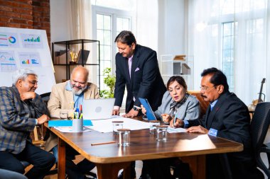 Hintli üst düzey iş adamları, Hindistan 'da üst düzey Asyalı iş adamları olarak birlikte çalışarak, rahat, modern kurumsal işyerlerindeki görevleri incelerken dizüstü bilgisayarları ve masa başındaki kağıtları kullanarak iş birliği yapıyorlar.