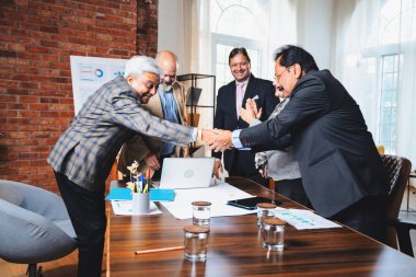 Hintli iş adamları anlaşmadan sonra el sıkışıyor. Hintli kıdemli Asyalı işadamı modern ofis toplantılarında gülümserken başarılı bir anlaşmayı imzalıyor.