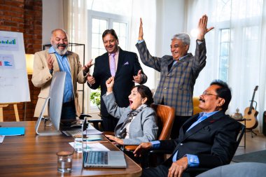 Hintli beş iş adamı laptopta çalışırken başarıyı kutluyor. Hintli üst düzey Asyalı işadamları modern ofiste masada otururken veya ayakta dururken kâr ve başarıyı alkışlıyor.