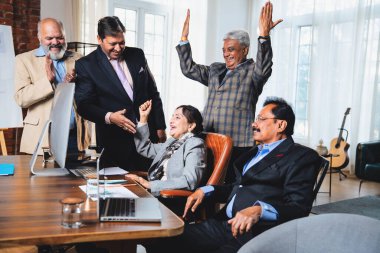 Hintli beş iş adamı laptopta çalışırken başarıyı kutluyor. Hintli üst düzey Asyalı işadamları modern ofiste masada otururken veya ayakta dururken kâr ve başarıyı alkışlıyor.