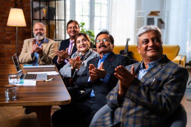 Hintli beş iş adamı sunum ve alkışları Hintli üst düzey Asyalı iş adamlarına yakın plan olarak görüyor ve modern ofis içinde masada otururken veya ayakta dururken başarılı brifing veriyorlar.