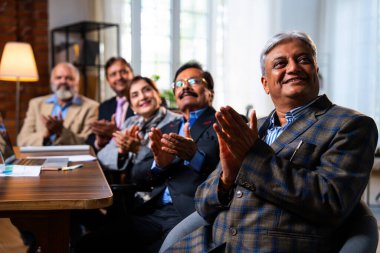 Hintli beş iş adamı sunum ve alkışları Hintli üst düzey Asyalı iş adamlarına yakın plan olarak görüyor ve modern ofis içinde masada otururken veya ayakta dururken başarılı brifing veriyorlar.