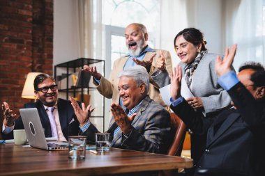 Hintli beş iş adamı laptopta çalışırken başarıyı kutluyor. Hintli üst düzey Asyalı işadamları modern ofiste masada otururken veya ayakta dururken kâr ve başarıyı alkışlıyor.