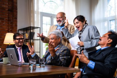 Hintli beş iş adamı laptopta çalışırken başarıyı kutluyor. Hintli üst düzey Asyalı işadamları modern ofiste masada otururken veya ayakta dururken kâr ve başarıyı alkışlıyor.