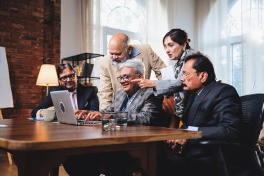 Hintli üst düzey iş adamları, Hindistan 'da üst düzey Asyalı iş adamları olarak birlikte çalışarak, rahat, modern kurumsal işyerlerindeki görevleri incelerken dizüstü bilgisayarları ve masa başındaki kağıtları kullanarak iş birliği yapıyorlar.