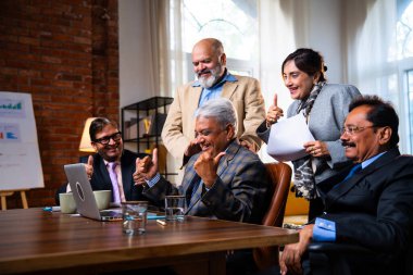 Hintli beş iş adamı laptopta çalışırken başarıyı kutluyor. Hintli üst düzey Asyalı işadamları modern ofiste masada otururken veya ayakta dururken kâr ve başarıyı alkışlıyor.