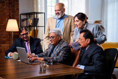 Hintli üst düzey iş adamları, Hindistan 'da üst düzey Asyalı iş adamları olarak birlikte çalışarak, rahat, modern kurumsal işyerlerindeki görevleri incelerken dizüstü bilgisayarları ve masa başındaki kağıtları kullanarak iş birliği yapıyorlar.