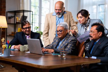 Hintli üst düzey iş adamları, Hindistan 'da üst düzey Asyalı iş adamları olarak birlikte çalışarak, rahat, modern kurumsal işyerlerindeki görevleri incelerken dizüstü bilgisayarları ve masa başındaki kağıtları kullanarak iş birliği yapıyorlar.