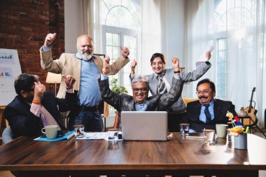 Hintli beş iş adamı laptopta çalışırken başarıyı kutluyor. Hintli üst düzey Asyalı işadamları modern ofiste masada otururken veya ayakta dururken kâr ve başarıyı alkışlıyor.