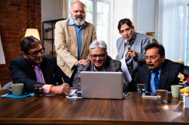 Hintli üst düzey iş adamları, Hindistan 'da üst düzey Asyalı iş adamları olarak birlikte çalışarak, rahat, modern kurumsal işyerlerindeki görevleri incelerken dizüstü bilgisayarları ve masa başındaki kağıtları kullanarak iş birliği yapıyorlar.