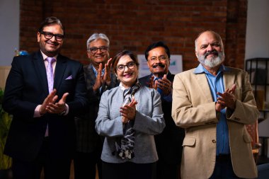 Hintli üst düzey iş adamlarının portresi gülümseyerek alkışlarken, Hintli üst düzey Asyalı yöneticiler modern şirket işyerindeki kameralara bakarak başarıyı alkışlıyor ve kutluyorlar.