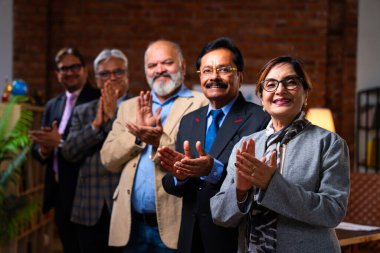 Hintli üst düzey iş adamlarının portresi gülümseyerek alkışlarken, Hintli üst düzey Asyalı yöneticiler modern şirket işyerindeki kameralara bakarak başarıyı alkışlıyor ve kutluyorlar.