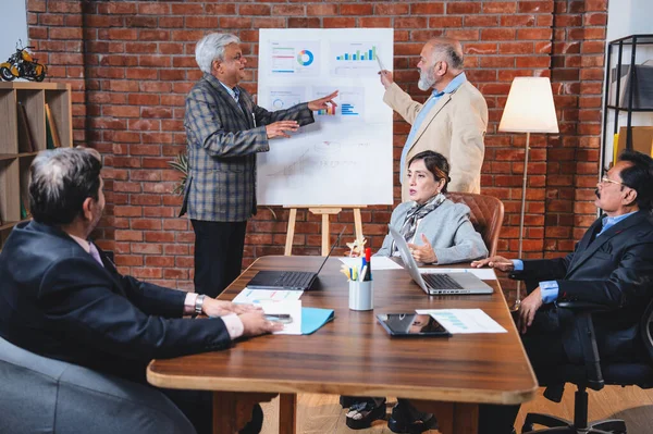 Hintli üst düzey iş adamları modern ofiste tartışırken Hintli üst düzey Asyalı iş adamları şirket büyümesi, strateji ve dizüstü bilgisayarla çalışırken masadaki kağıtlar hakkında hararetli tartışmalara girişiyorlar.