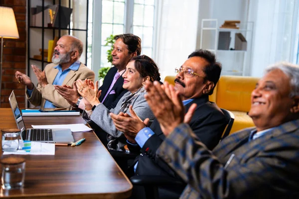 Hintli beş iş adamı sunum ve alkışları Hintli üst düzey Asyalı iş adamlarına yakın plan olarak görüyor ve modern ofis içinde masada otururken veya ayakta dururken başarılı brifing veriyorlar.