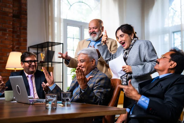 Hintli beş iş adamı laptopta çalışırken başarıyı kutluyor. Hintli üst düzey Asyalı işadamları modern ofiste masada otururken veya ayakta dururken kâr ve başarıyı alkışlıyor.