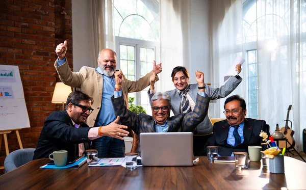 Hintli beş iş adamı laptopta çalışırken başarıyı kutluyor. Hintli üst düzey Asyalı işadamları modern ofiste masada otururken veya ayakta dururken kâr ve başarıyı alkışlıyor.