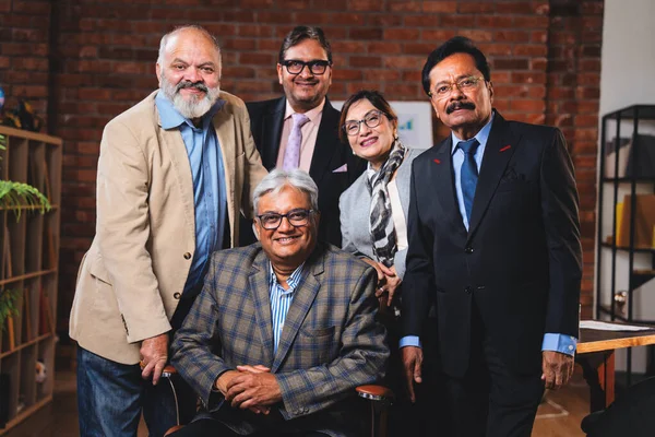 Hintli üst düzey iş adamlarının portresi Hintli üst düzey Asya yöneticileri kılığına girmiş patronun kanat koltuğunda otururken modern şirket ofisinde poz verirken kameraya gülümsüyor.