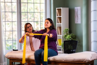 Fizyoterapist Hintli kadın hasta triseps ve omuz güçlendirme egzersizleri yapıyor modern klinikte direnç bandını kullanarak rehabilitasyon ve iyileşme için kıdemli rehberlik altında