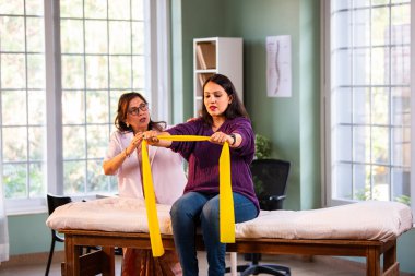 Fizyoterapist Hintli kadın hasta triseps ve omuz güçlendirme egzersizleri yapıyor modern klinikte direnç bandını kullanarak rehabilitasyon ve iyileşme için kıdemli rehberlik altında